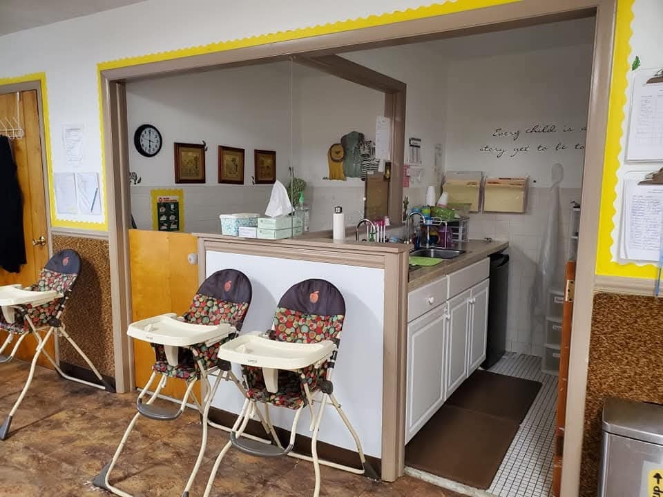 Infant classroom kitchen area with high chairs and a 'Every child is a story yet to be told' wall quote