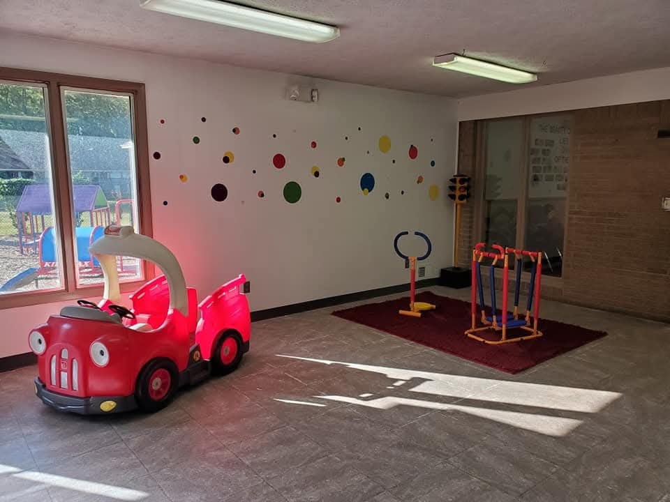Bright classroom room with a red ride-on car toy, exercise equipment, and colorful dot wall art