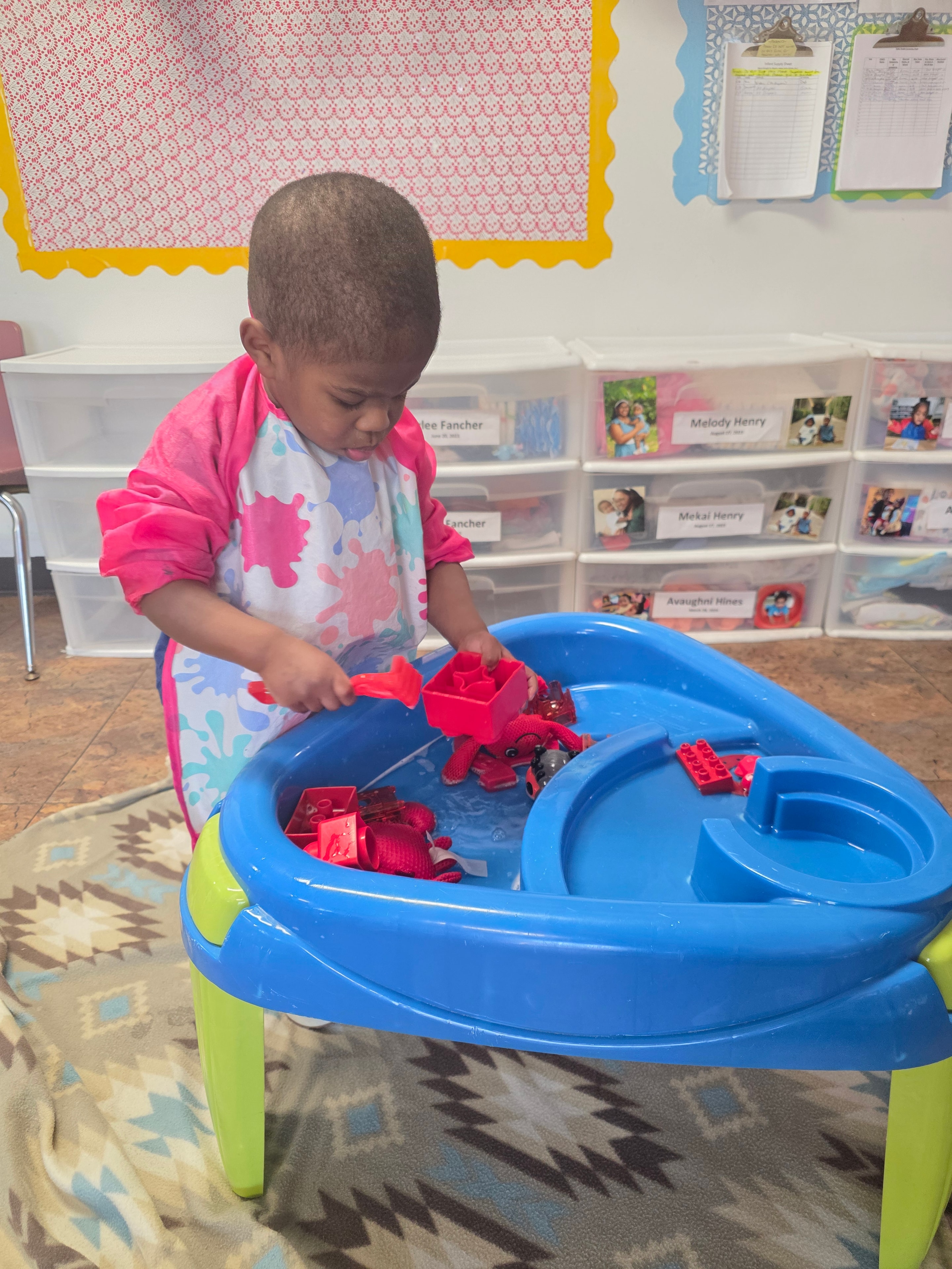 Toddler exploring red sensory toys at the water and activity table