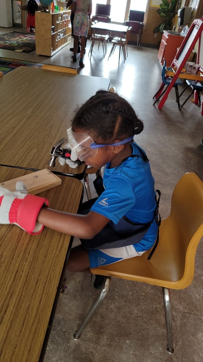 School-age child wearing safety goggles and gloves working on a woodworking project in the classroom