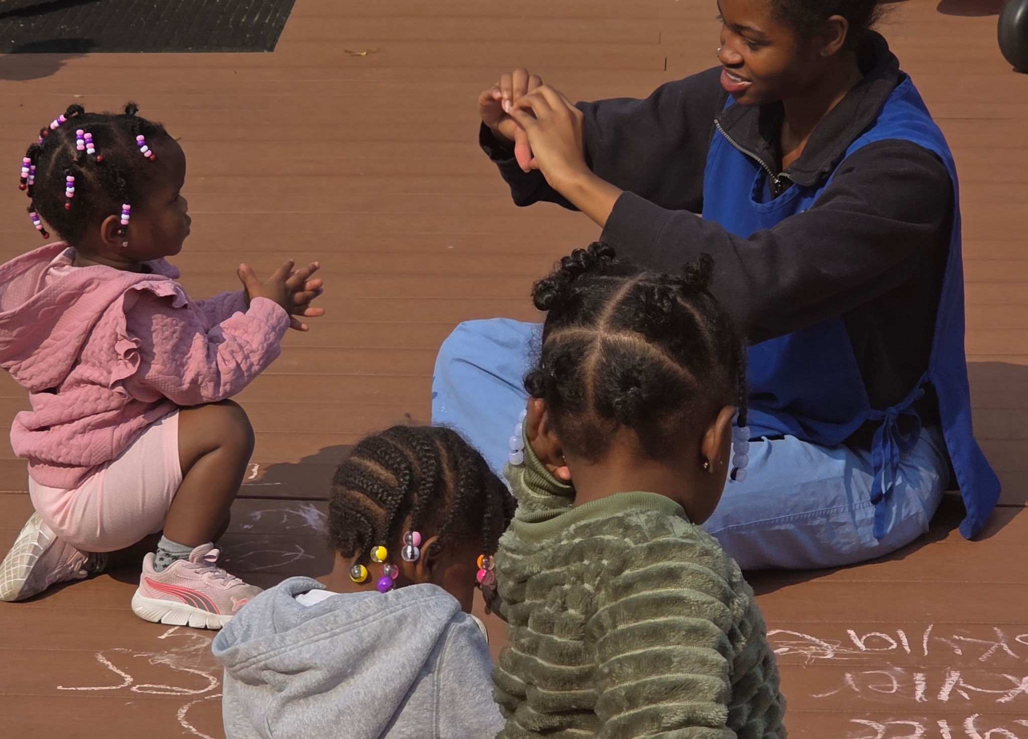 Teacher engaging with children on the outdoor deck with chalk drawings