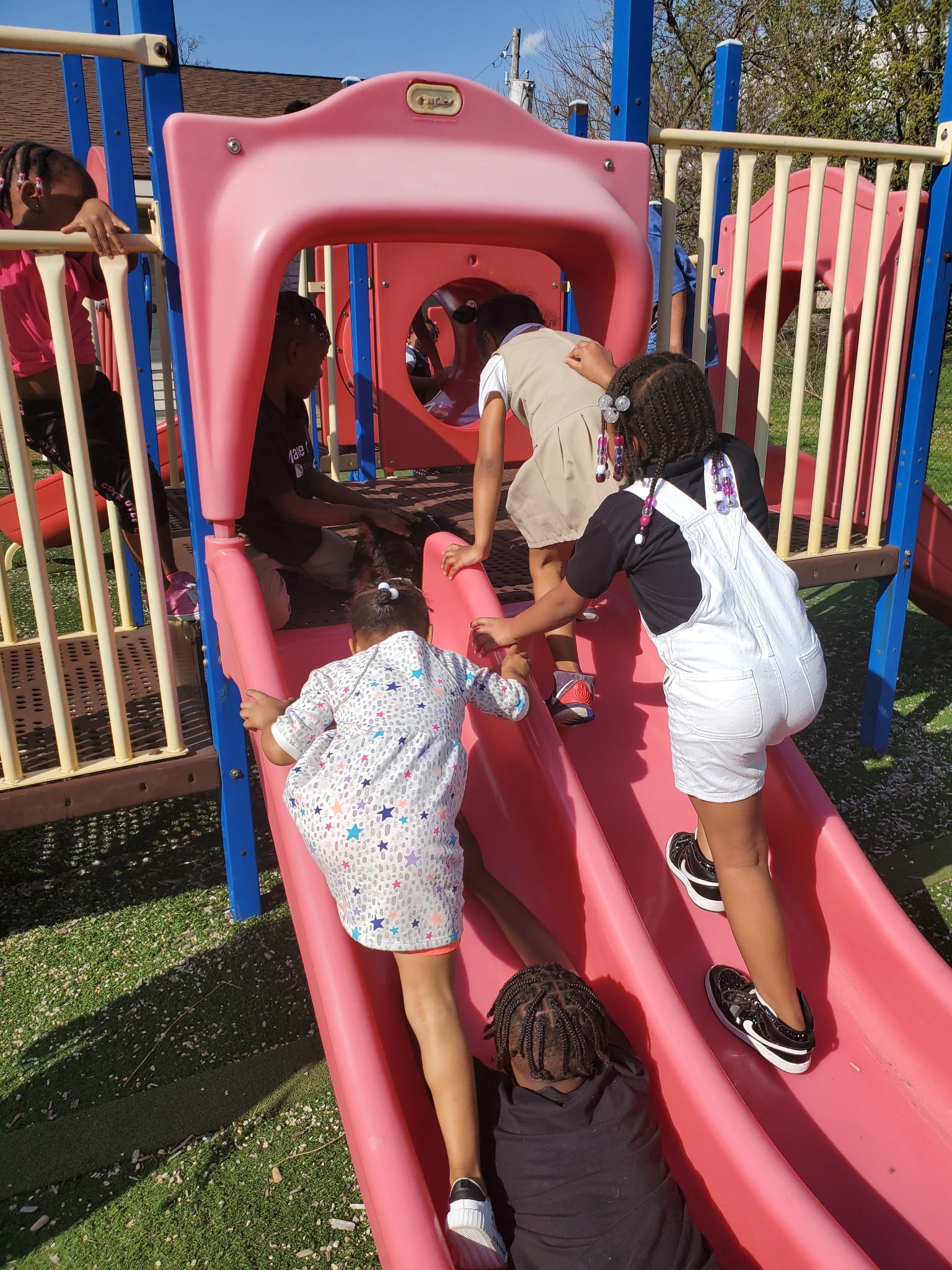 Group of children of mixed ages climbing and playing together on the pink playground slide
